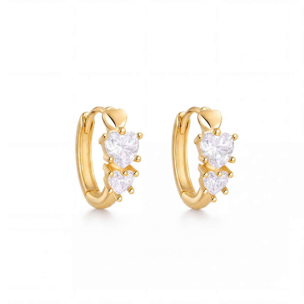 A pair of gold huggie hoop earrings with three clear heart-shaped gemstones on each earring, set against a plain white background.