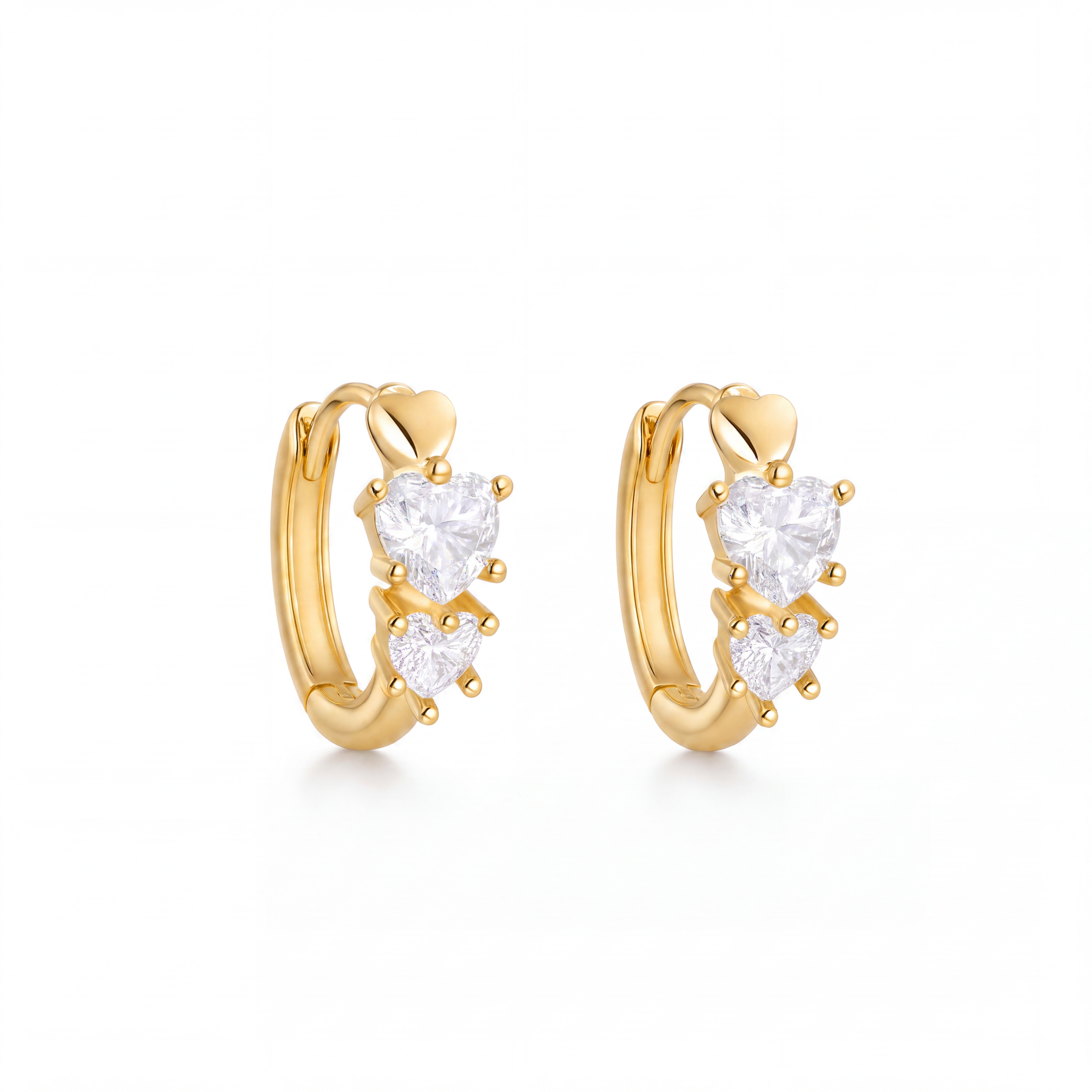 A pair of gold huggie hoop earrings with three clear heart-shaped gemstones on each earring, set against a plain white background.