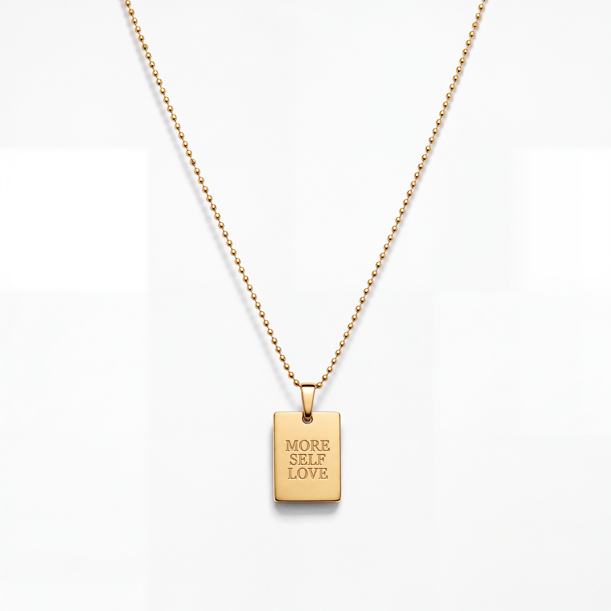 A gold ball-chain necklace with a rectangular gold pendant engraved with the words 'MORE SELF LOVE' in all caps, shown against a clean white background.