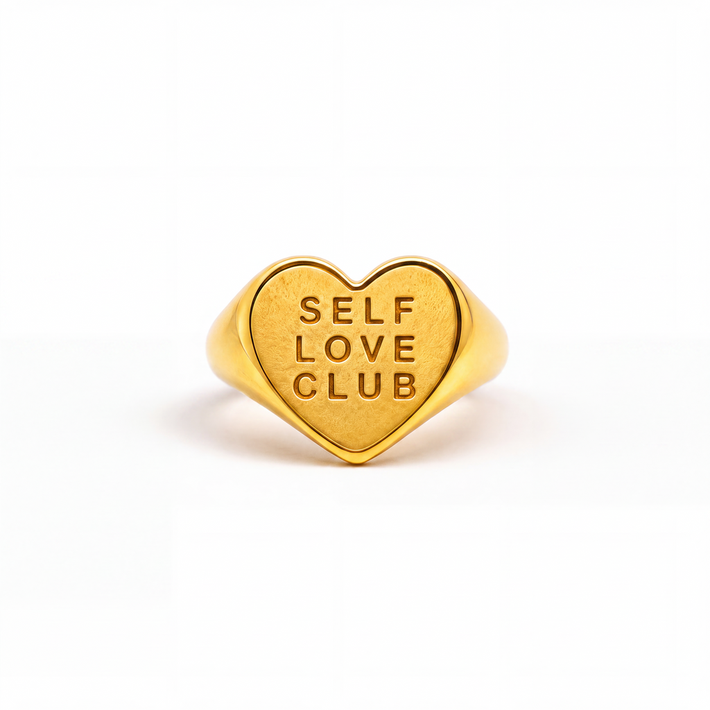 A gold heart-shaped signet ring engraved with the words 'SELF LOVE CLUB' in a warm yellow-gold finish, centered on a clean white background.