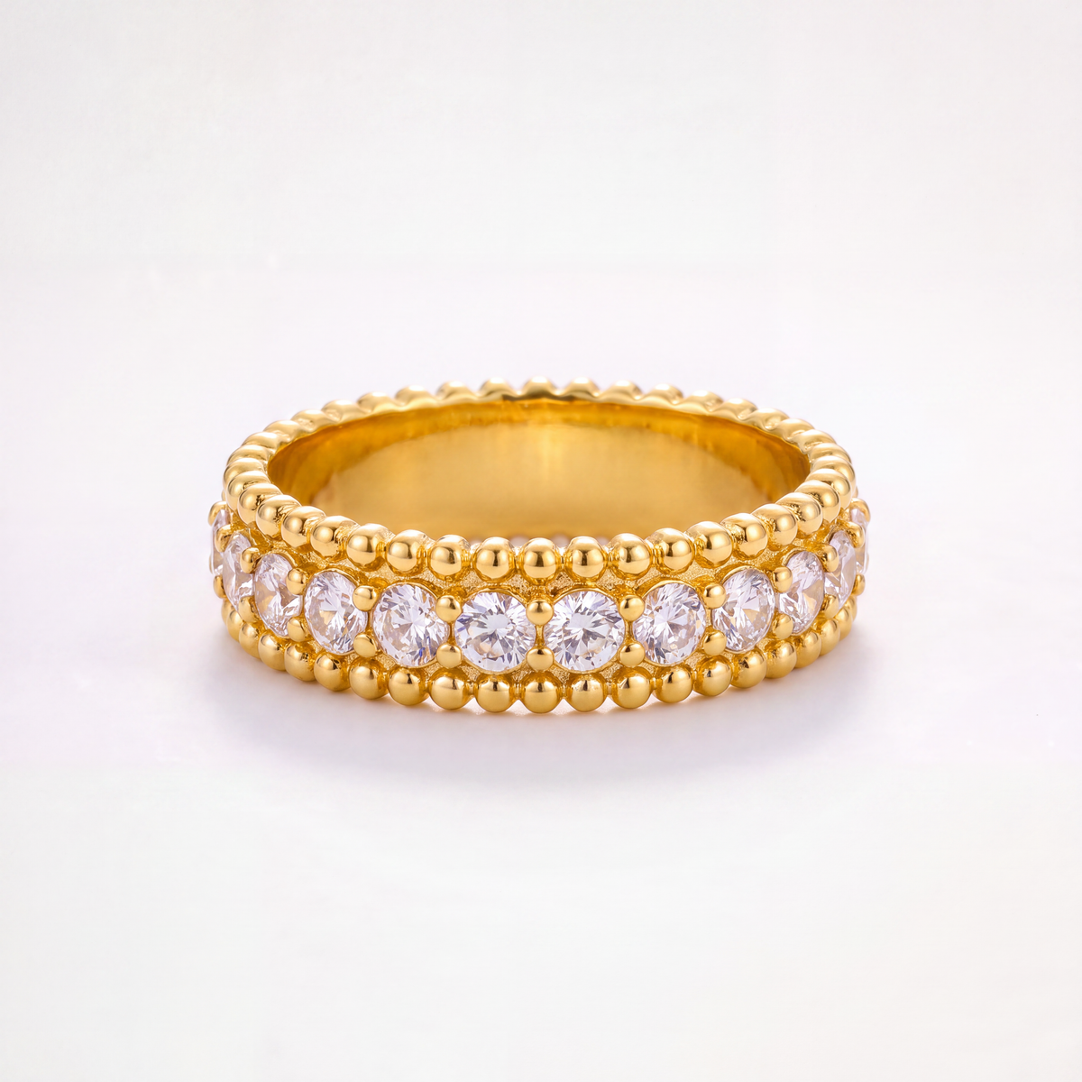 A yellow gold eternity ring featuring two rows of round brilliant-cut clear gemstones and a beaded border, set against a clean white background.