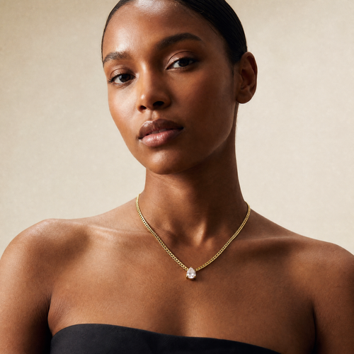 Woman wearing a gold necklace with a clear pendant against a neutral background