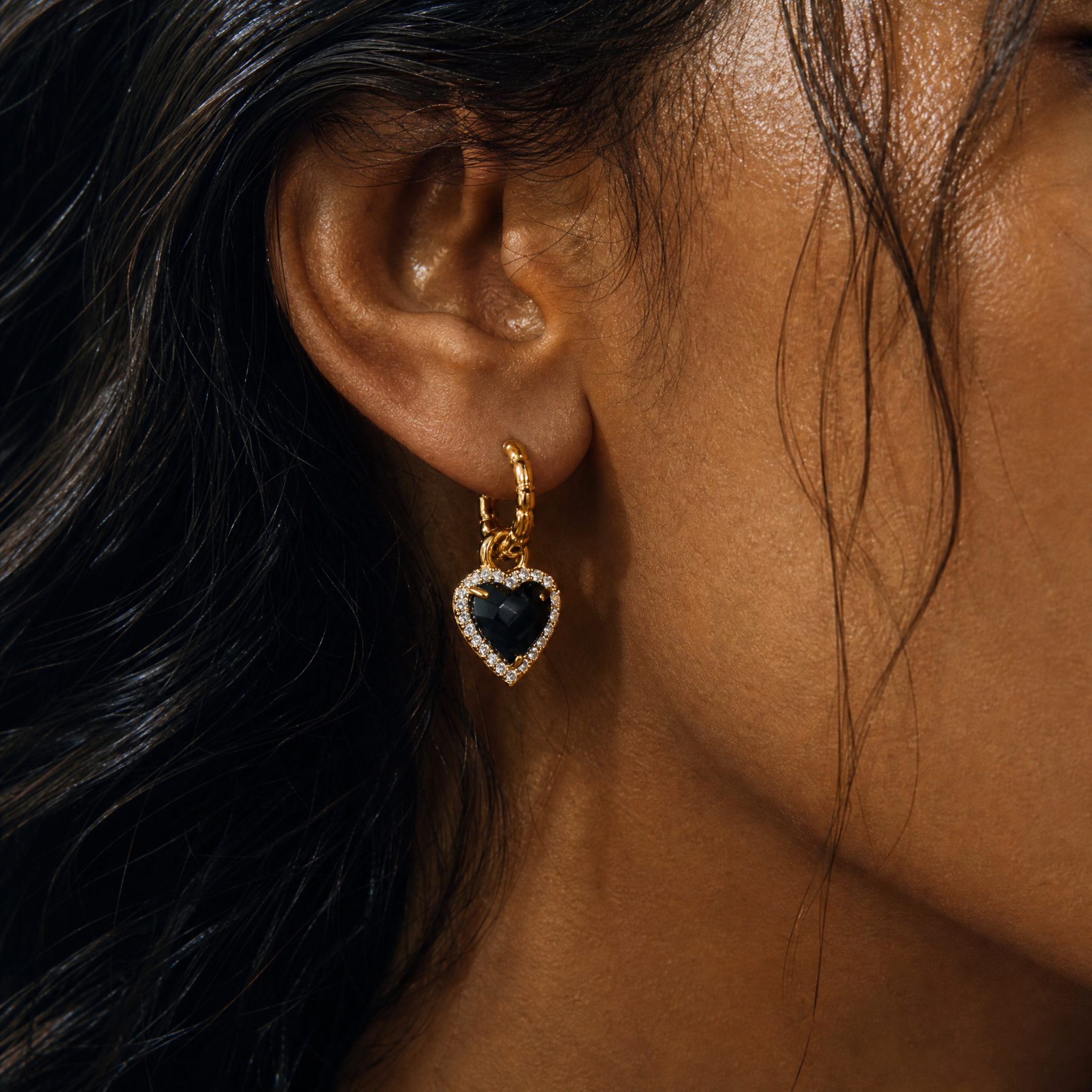 Heart-shaped earring with a black gemstone worn by a person with dark hair.